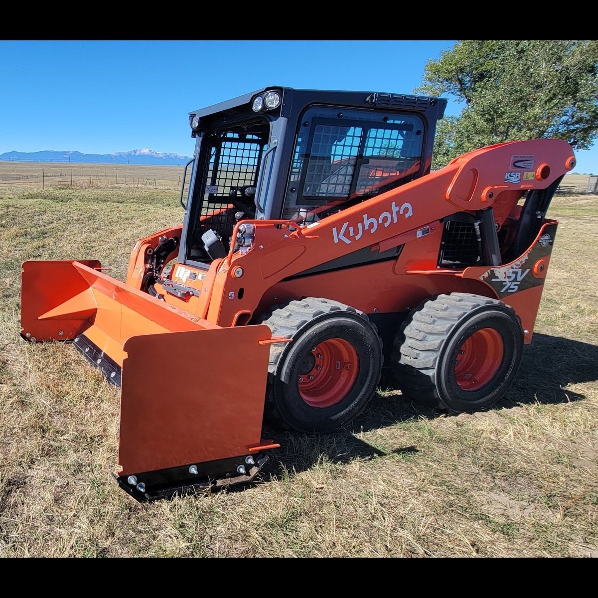 Kubota SSV75 skid steer with 92-inch orange snow pusher, front three-quarter view