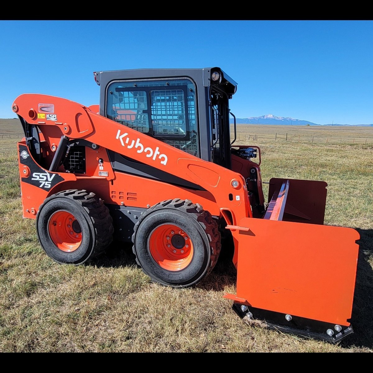 Kubota SSV75 skid steer with 92-inch orange snow pusher, side profile